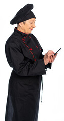 woman chef in black uniform. apron, shirt, hat. elderly woman. a food preparation specialist maintains social networks, responds to messages, online ordering. white background, isolated