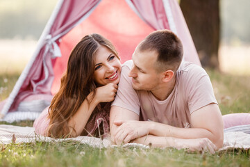 Relaxed young couple sitting near wigwam in park on sunny day. summer holiday vacation. man and woman are hugging outdoors and huving fun. © Andriy Medvediuk