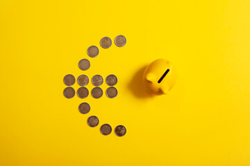 Top view of euro symbol made from euro coins with piggy bank beside it and yellow background