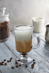 Coffee in a tall glass with cream and coffee beans on the background of a wooden table.