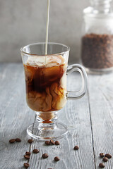 Coffee in a tall glass with cream and coffee beans on the background of a gray wooden table.