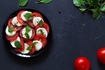 tomato and basil.Italian caprese salad with green on the black plate with copy space. sliced red tomatoes, mozzarella cheese, green basil, olive oil on a dark background. fresh salad.top view.