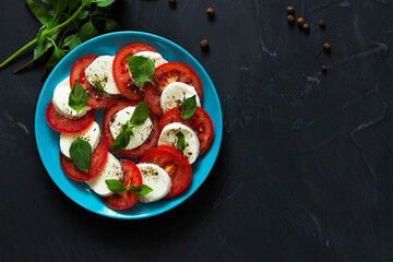 tomatoes and mozzarella.Italian caprese salad with green on the blue plate with copy space. sliced red tomatoes, mozzarella cheese, green basil, olive oil on a black background. fresh salad.top view.