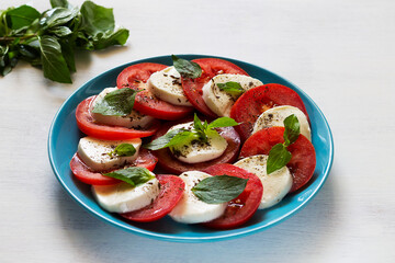 Italian caprese salad with fresh green on the blue plate. sliced tomatoes, mozzarella cheese, green basil, olive oil on a white background. fresh salad with copy space.
