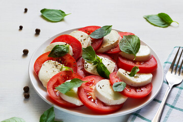 tomato salad with mozzarella and basil.Italian caprese salad. sliced tomatoes, mozzarella cheese, green basil, olive oil on a white background. fresh salad with copy space.