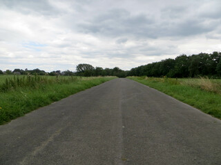 Longue route au milieu des prés sous un ciel nuageux