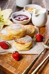 Cottage Cheese Pancakes with fresh strawberries and jam. Curd Cheese Pancakes on a wooden board sprinkled with powdered sugar. Delicious homemade breakfast or snack. Vertical shot