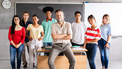 Mature male high school teacher with his multiracial group of teen students looking at camera. Horizontal banner image.