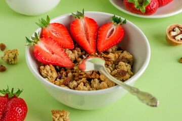 Homemade baked muesli, nuts, fresh strawberries on a green background. Healthy breakfast in a white bowl with natural granola.