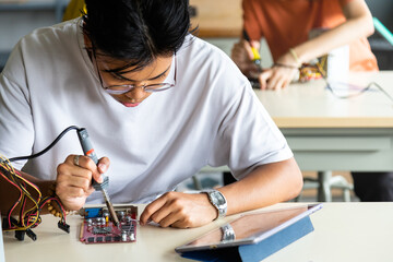 Close up of teen asian boy in electronics class working on a project alone.