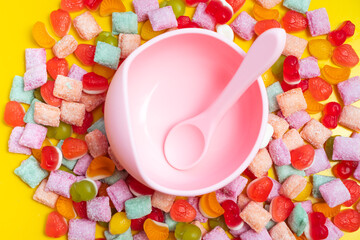 Children's tableware silicone bowl with spoon. Serving baby food, kid dishware.Pink silicone bowl and spoon are in a heap of sweets and marmalade. bright, colorful photo flatly