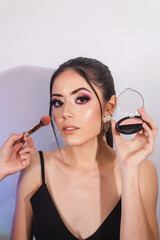 Beautiful girl holding makeup products on white background. Makeup artist blurring cheeks.