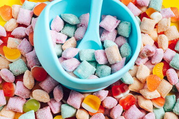 Children's tableware silicone bowl with spoon. Serving baby food, kid dishware.blue silicone bowl and spoon are in a heap of sweets and marmalade. bright, colorful photo flatly