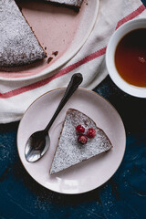 Chocolate cake decorated with cranberries and powdered sugar, kladdkaka with a cup of tea on a blue background.  Swedish desert. White dish towel. 