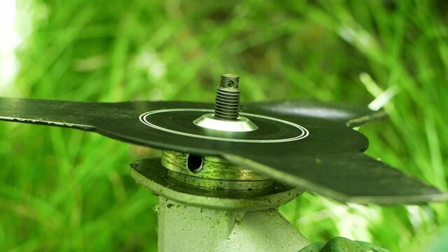 A man puts a knife on a lawnmower before cutting grass outside. Trimmer in the hands of a man, assembly and cleaning. Grass trimmer