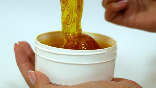 The beautician removes sugar paste from a white jar with a wooden spatula before the sugaring procedure. Hair removal procedure with natural sugar paste. Sugaring is a beauty salon.