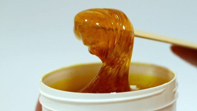 The beautician removes sugar paste from a white jar with a wooden spatula before the sugaring procedure. Hair removal procedure with natural sugar paste. Sugaring is a beauty salon.