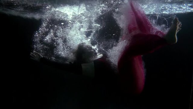 a blonde in a red dress falls into the dark water and swims in bubbles