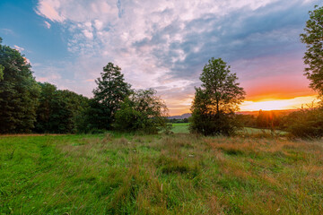 Fototapeta na wymiar Colorful sunset on a warm summer evening over the rolling hills in Limburg. The sky showed amazing colours which gives a natural contrast to the green colours of the forest and meadow