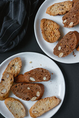 Classical and chocolate biscotti with almonds on two white plates. Black backround. 