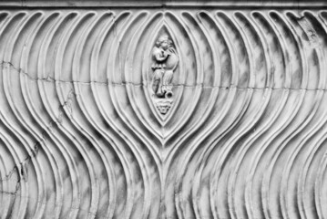 Black and white photo of decorated marble wall carved on a pattern of waves surrounding the figure of a man 