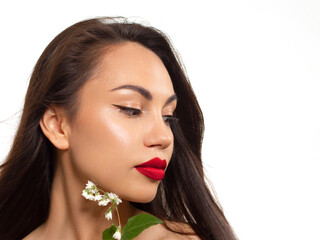 Fototapeta premium Close-up beauty of female face withevening make-up. Black arrows on the eyes and extremely long eyelashes, on full pink lips matte scarlet lip color. Well-groomed skin. white flowers