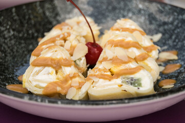 Fresh pink pancake rolls are on a plate. Traditional sweet dessert contains cream cheese, mango, banana, pear, caramel, sauce, almonds; cherry.
