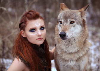Warrior girl with painted face with grey wolf in winter forest