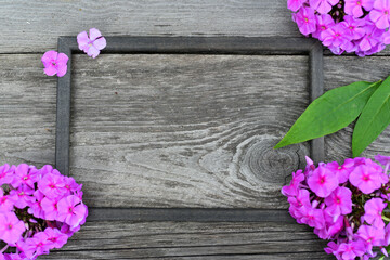 A dark wooden frame on a wooden table, framed with phlox and leaves.
