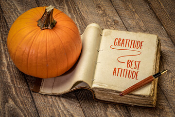 gratitude - best attitude, inspirational handwriting in a retro, leatherbound journal with a pumpkin against rustic wood, fall holiday and Thanksgiving theme