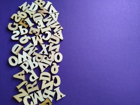 wooden letters of the alphabet scattered on a purple background with space for text. High quality photo