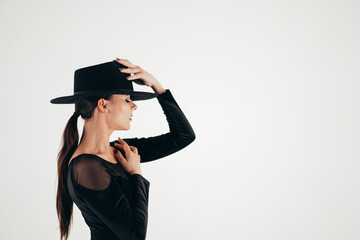 Charming woman posing with black hat on white background. Femme fatale costume, stylish outfit. Sexy model dancer.