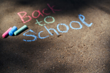 Blurred background. Inscription Back to school with colored crayons on the asphalt