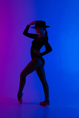 Fototapeta na wymiar Contemporary ballet dancer woman in hat posing on multi-colored gradient pink blue background. Professional ballerina in sexy costume of femme fatale, solo performance.