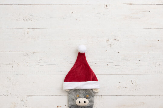Children's knitted hat with a picture of a bull and wearing a Christmas hat of santa claus on the background of a white wooden table.