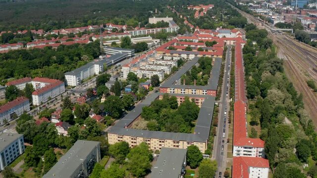 Fly above rows of buildings in old housing estate. Railway line extending to more tracks. Tilt up revealing of large city. Berlin, Germany