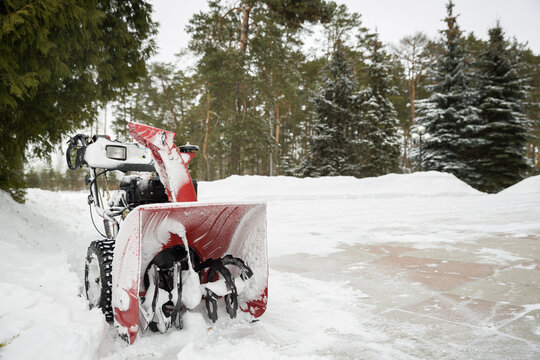 A red snow-covered snow blower stands on the road after clearing the area. Clearing the area from snowfall.