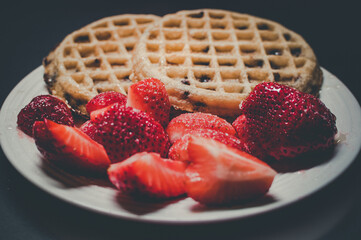 The chocolate chips warm waffle with fresh strawberries on the side for breakfast.. White plate. Black background. Selective focus.