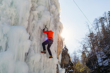 Aerial shot of a frozen ice waterfall, and the male climber progresses up the slope, while rope attached to his harness prevents him from falling