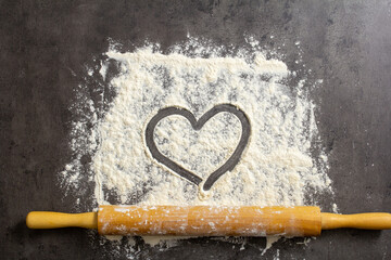 on a background of flour, a heart is drawn on a dark table, a rolling pin and ears of wheat