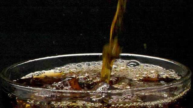 Pour cola water into a glass with ice. until a bubble splashed out , Cola is a soft drink  soda carbonated. It's an unhealthy drink, a lot of sugar, Close-up,  liquid pouring into glass