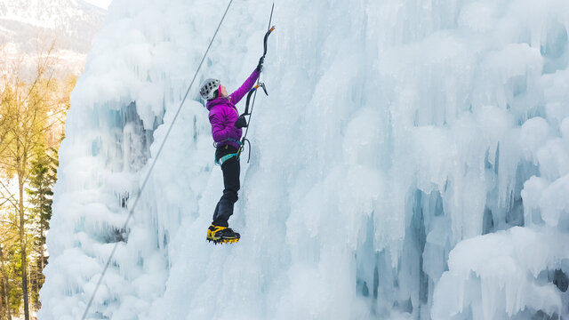 Female ice climber silhouette swinging ice axes on her way up vertical ice waterfall, side view