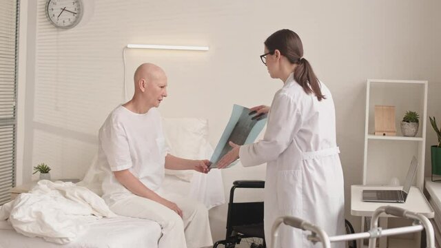Panning medium slowmo shot of female doctor showing happy cancer patient her x-ray image telling good news about results