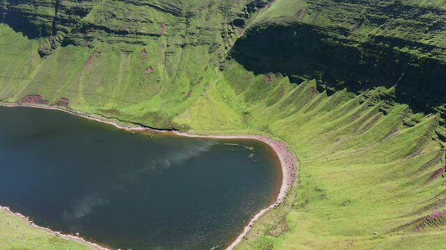 Aerial view of a lake at the foot of large cliffs (Llyn y Fan Fach)