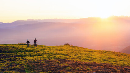 Mother and daughter cycling on mountain bikes at a sunset in mountains.