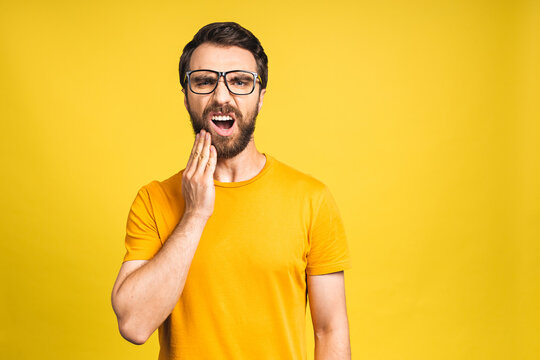 Close up portrait of nervous unhappy troubled handsome bearded man touching his cheek he has toothache isolated on yellow background copyspace.