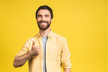 Happy young man. Portrait of handsome young bearded man smiling while standing isolated over yellow background. Thumbs up.