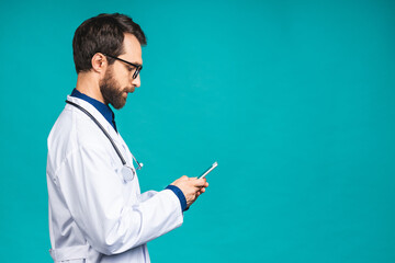 Young doctor texting on a smart phone isolated on a blue background. Using mobile phone.