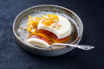 Modern style traditional blancmange almond pudding with mango compote and quince gelee coulis served as close-up on a design plate on black background