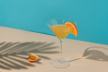 Tropical cocktail with orange slice and palm leaf shadow on vivid blue background. Minimal summer drink composition. Flat lay.